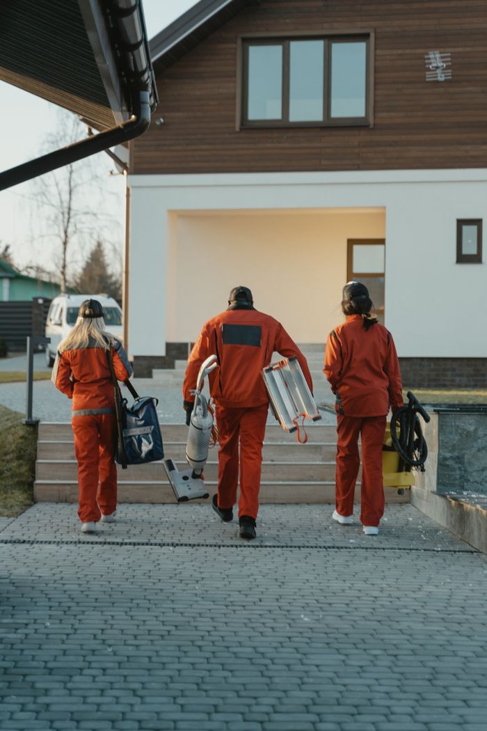 creative-03 A cleaning team dressed in red uniforms, carrying their equipment, is walking toward the outside of a modern home.